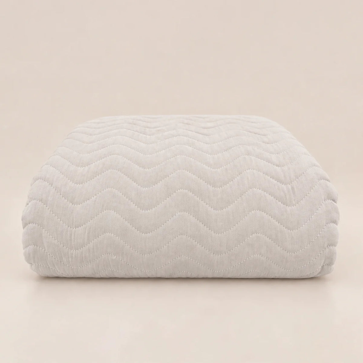 Cubrecama de entretiempo en tono gris muy claro hueso doblado mostrando el pespunte en relieve zig zag.