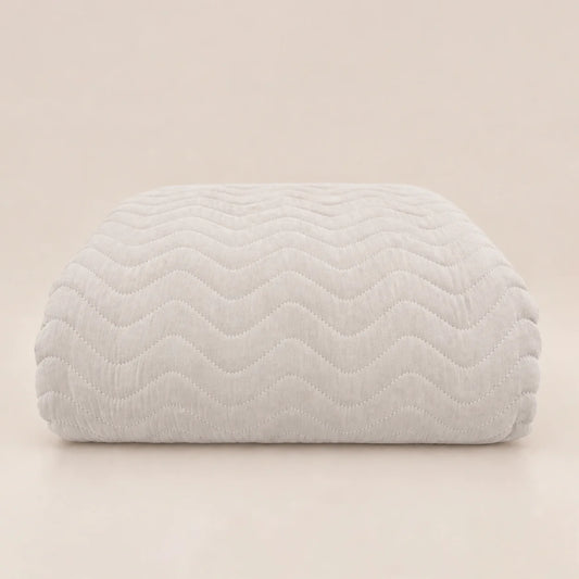 Cubrecama de entretiempo en tono gris muy claro hueso doblado mostrando el pespunte en relieve zig zag.