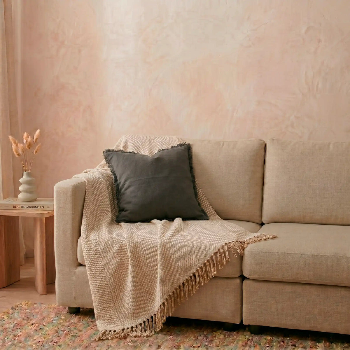 Funda de cojín gris oscuro con flecos de Omahome decorando un sofá moderno, aportando carácter y contraste al salón.