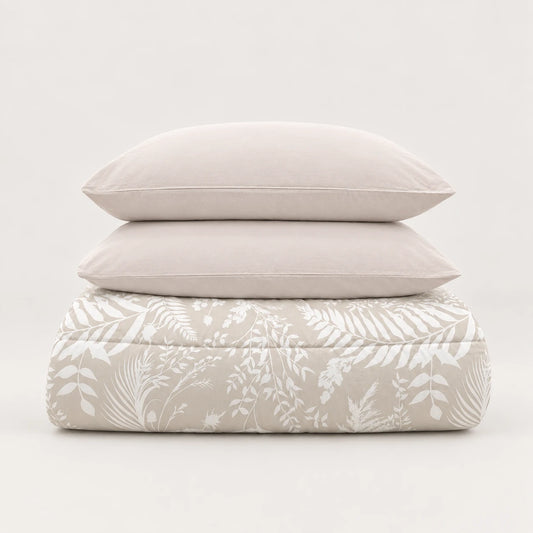 Edredón de invierno beige con estampado de hojas blancas doblado impecablemente, coronado por dos fundas de almohada a juego.