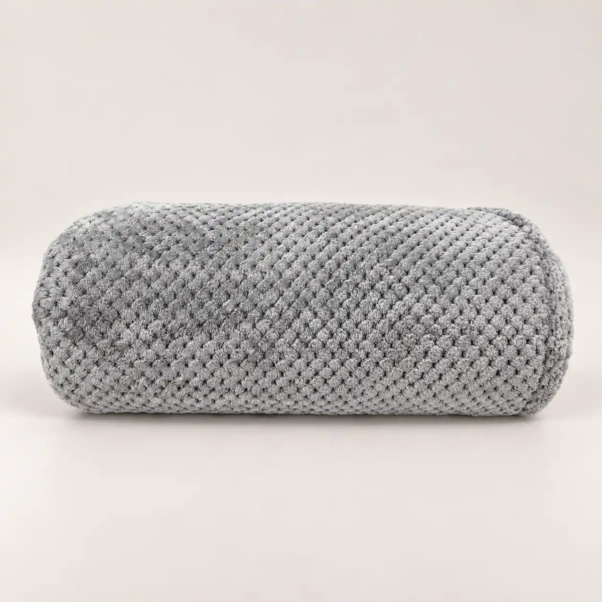 Manta polar fina y extra suave de color gris claro doblada sobre madera, mostrando su relieve texturizado.