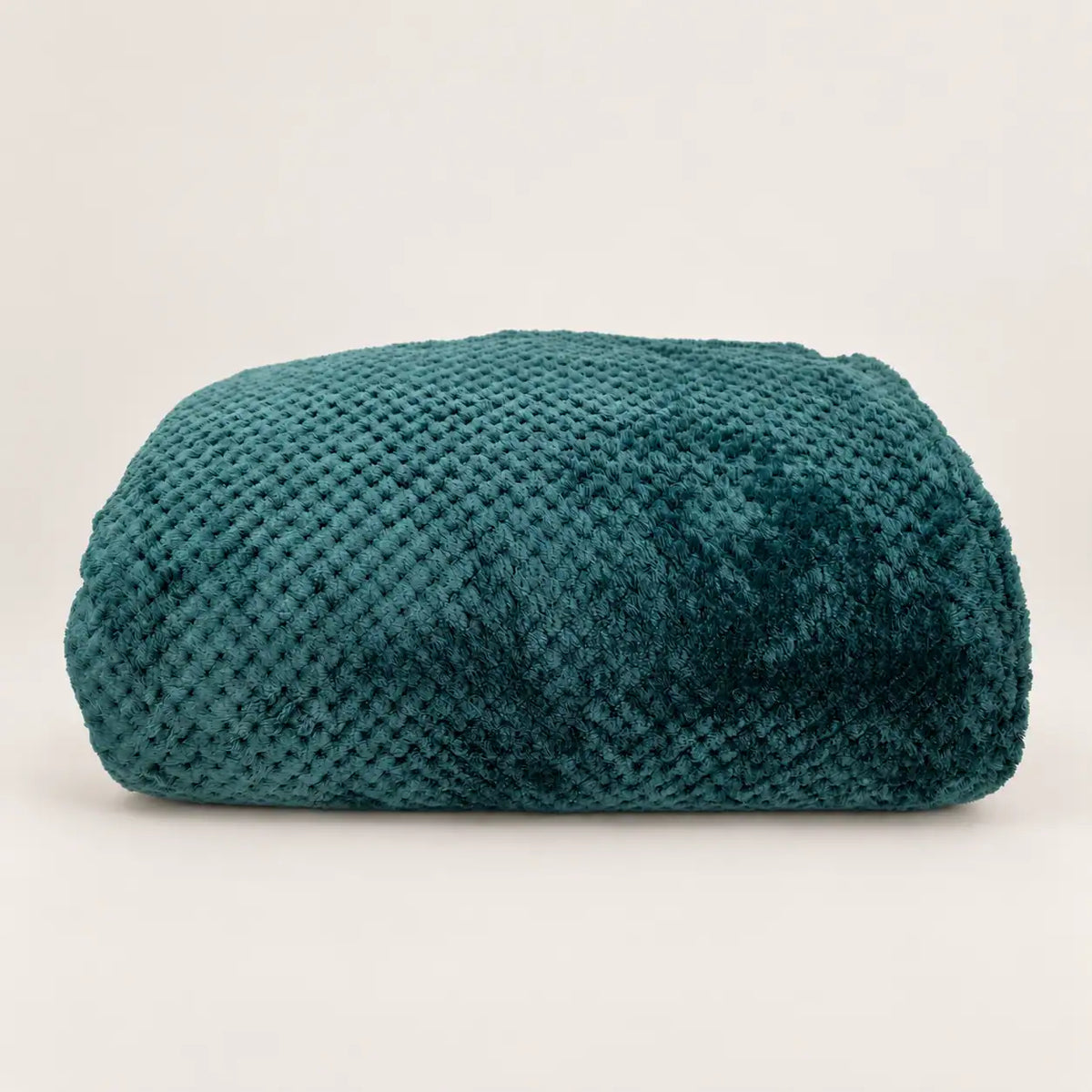 Manta polar fina y extra suave de color verde oscuro doblada sobre madera, mostrando su relieve texturizado.