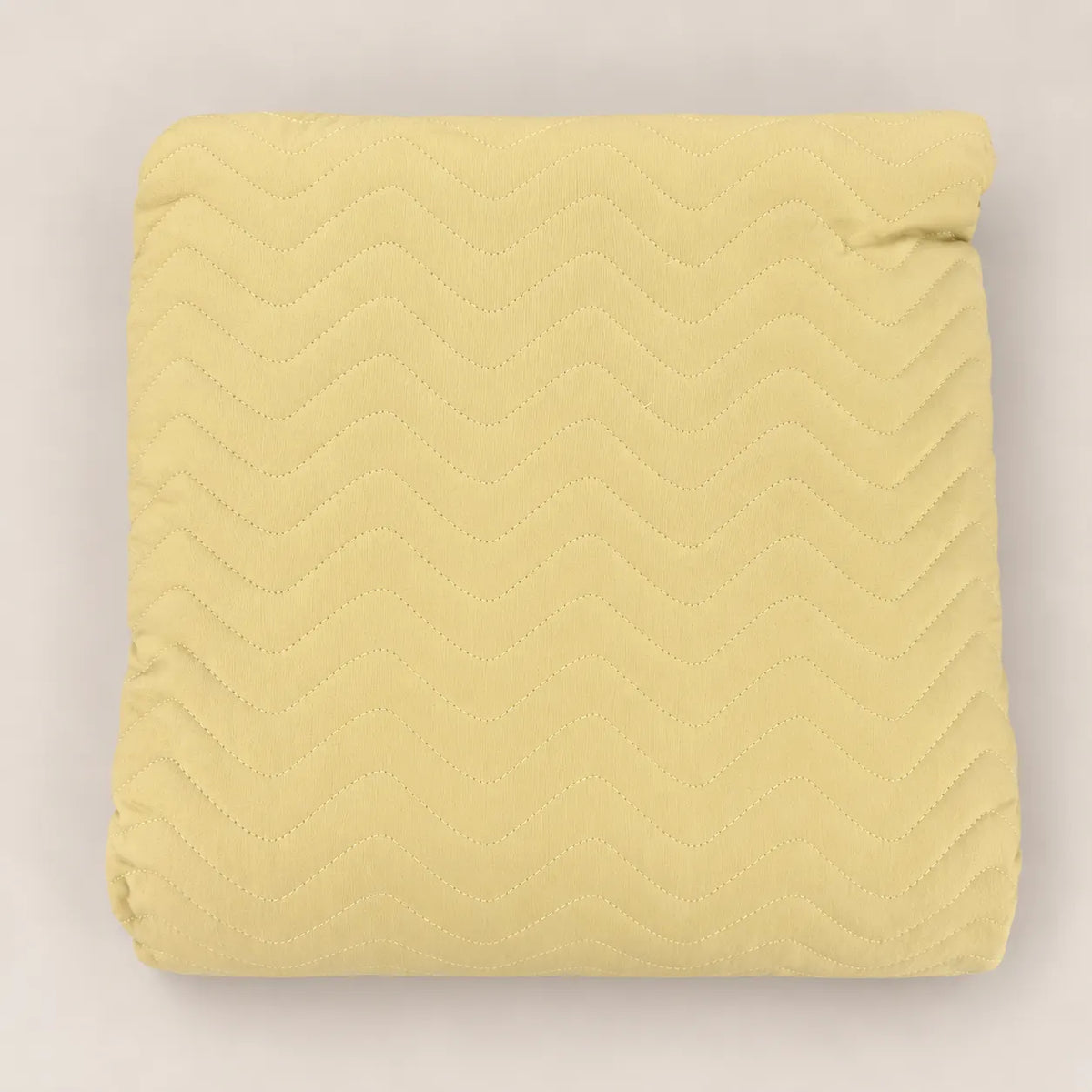 Cubrecama fino de primavera en tono amarillo mostaza doblado mostrando el estampado en relieve zig zag.