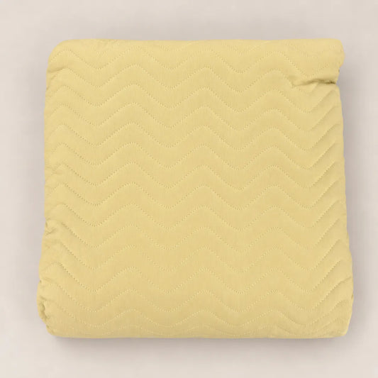 Cubrecama fino de primavera en tono amarillo mostaza doblado mostrando el estampado en relieve zig zag.